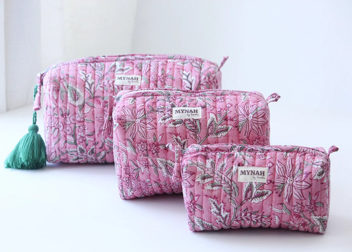 Three pink floral-patterned fabric pouches of varying sizes, each labeled MYNAH, are arranged on a white surface. The largest pouch has a green tassel attached to its zipper.