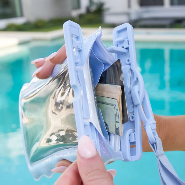 A person holds open a Mist Twinkle Wavy Waterproof Floating Phone Pouch in light blue, containing cash and cards, beside a swimming pool.
